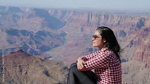 Grand Canyon, Arizona - tourist woman, sitting on a rock contemplating Grand Canyon scenic view