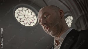 Low angle medium closeup of middle aged bald headed Caucasian pastor reading holy book in Catholic Church aloud