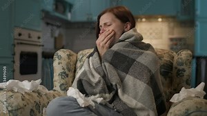 Sick woman feeling cold at home. 30s lady wrapped in blanket trying to get warm on couch. Lack of heating in apartments.