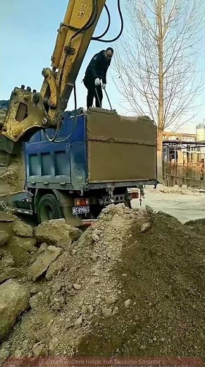 Excavator Shovels Soil: Worker Directs Loading on Site!