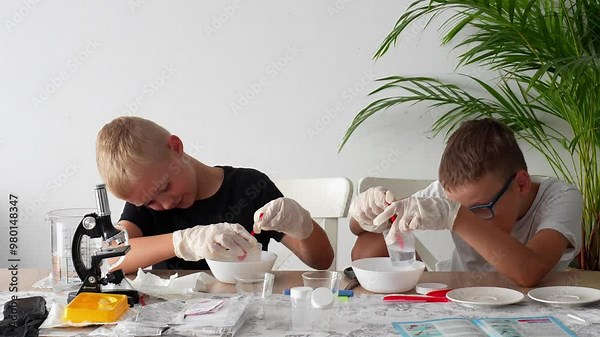 Two boys work together to conduct an experiment to grow crystals by mixing powder and water in a beaker. Concept of scientific discovery, teamwork and hands-on learning. High quality 4k footage