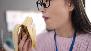 Young chinese woman preschool teacher eating banana at kindergarten