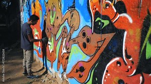 Graffiti Artist Painting On The Street Wall. Handsome Man with aerosol spray bottle spraying with colorful paint, Urban Outdoors Art Concept. Slow motion. Gimbal shot