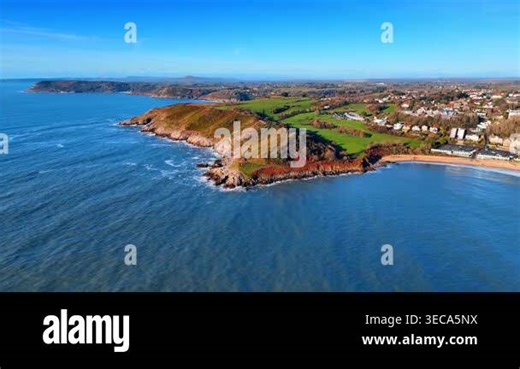 Panoramic aerial shot of Gower Peninsula coastline and golf course. Drone perspective of rocky headland, green fields, golf course and coastal town under clear blue sky in Wales Stock Video Footage - Alamy