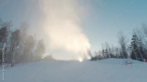 Snow cannon generates a lot of artificial snow at ski-resort in early winter. A lot of fresh artificial snow powder is in the air against morning sun