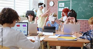 Elementary school age children sitting in VR glasses and learning to use virtual reality with help of teacher during chemical lesson. Concept of modern technology in education.