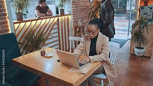 Afro-american young attractive smart man walking inside cafe and greeting with employer businesswoman sitting for corporate job interview in the cafeteria. Business, technology and job concept