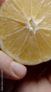 Vertical video. I squeeze the juice from half a lemon. Slow-motion view from below, drops appear to be flying towards you. Close-up.