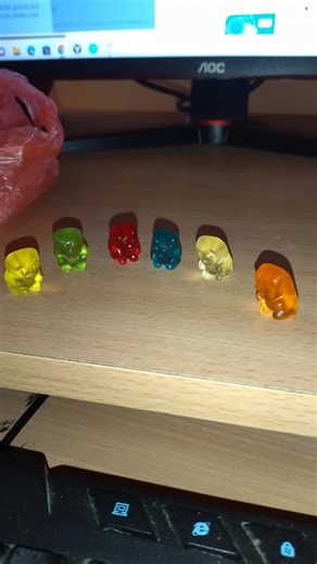 🍬💻 A cinematic funny scene on a messy computer desk at night. Colorful gummy bears suddenly come to life and start having wild adventures around the desk. One gummy bear surfs on a computer mouse, another climbs a keyboard like a mountain, two gummy bears ride a spinning office chair wheel like a carousel. One bear dives into a mug of coffee like a swimming pool, another slides down a charging cable like a zipline. #gummy #gummybears #funny #desk #miniworld