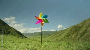 Pinwheel is slowly spinning with wind energy, background mountains and sky