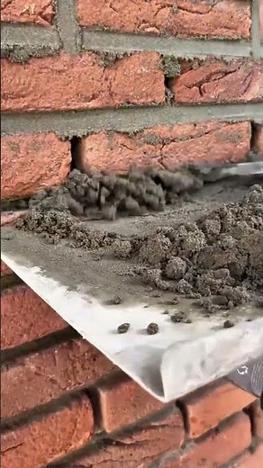 filling gaps between red bricks with cement mortar using a small trowel to strengthen the wall