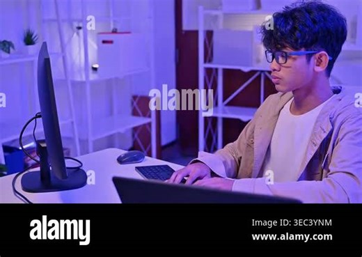 Focused young Asian male programmer wearing glasses writing code on computer monitor in a dark room with blue neon light. Smart teenager playing video games or studying cybersecurity Stock Video Footage - Alamy