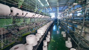 A facility with working machines, spooling threads onto bobbins. Weaving machine working at textile fabric.