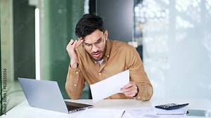 Frustrated financier unhappy with bad financial results checking documents on laptop computer looking at camera. Confused puzzled employee having difficulty with paper work sitting in business office