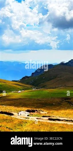 Grassy mountain ridge under a dramatic cloudy sky with industrial ski lift infrastructure and distant peaks. Vertical video Stock Video Footage - Alamy