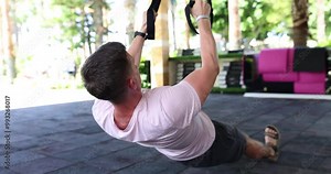 Male person uses training machine to pump up arms in light home gym. Fit man in sportswear uses exercise equipment for intensive workout slow motion