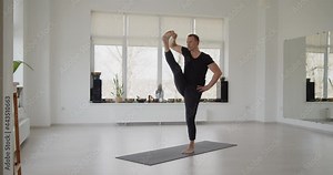 Professional trainer practices flow yoga in private class. Adult man makes yoga asanas on a mat in white bright studio. Fitness, healthy lifestyle and wellness concept.