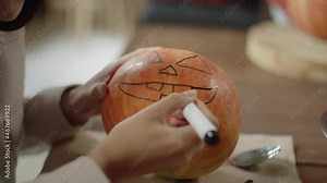 An adult lady is finishing to draw a jack face on a halloween pumpkin Stock Video