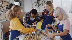 Multi-cultural team of trainees in workshop learning how to assemble hand built bamboo bicycle frame together - shot in slow motion