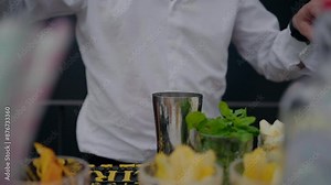 Bartender preparing a cocktail, using a muddler, with fresh ingredients on the counter.