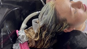 Young woman in hairdresser's salon and her stylist washing her hair for hair treatment. Hairdresser, client and cosmetics. Washing and lightening.