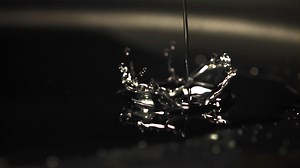 Super slow motion jet oil falls on the pan with splashes. On a black background. Filmed on a high-speed camera at 1000 fps.