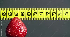 Fruit diet concept - a strawberry on a fork slides under a yellow measuring tape as an indicator.