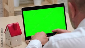 Man using green screen chroma key laptop near house model. Buying and selling home via internet, insurance online, rent and booking apartment