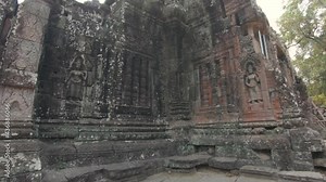 Backwards pan away from a richely detailed wall that's part of the ruins in Angkor Wat