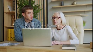 Elderly businesswoman communicates with middle aged businessman, discussing working issues, look at laptop screen, management distributes tasks for employee