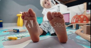 Closeup of cute child foot moving fingers laying on the floor in home barefoot. Carefree childhood enjoying in kid room after playing with toys