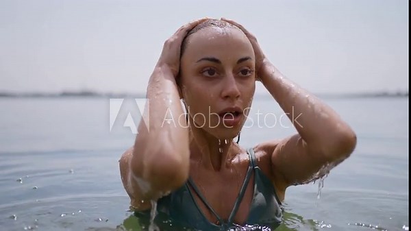 Beautiful woman comes up from lake and water falling down from her face, slow motion