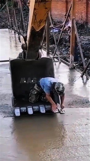 Un ouvrier du bâtiment s'agenouille dans le godet d'une pelleteuse pour niveler du béton frais.