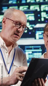 Vertical video Software developers in high tech establishment, completing tasks on tablet while running scripts on laptop terminal. Proactive programmers amidst server rows, accessing databases and