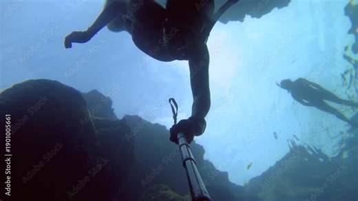 selfie of an asian female woman wearing bikini snorkel mask fin free diving down into the water from bottom to top view in dark atmosphere surrounding by coral reef look up to diver silhouette surface