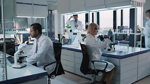 Team of Medical Research Scientists Conduct Experiments with Help of Microscope, Test Tubes, Micropipette and Writing Down Analysis Results on a Computer. Modern Biological Applied Science Laboratory.
