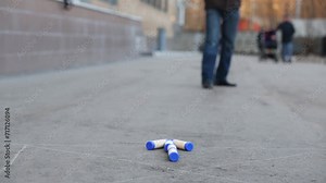 Man throwing stick for arrow of little sticks on pavement.