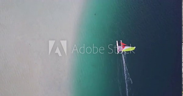 Aerial tracking over a windsurfer sailing across topical waters with brightly lit sand, gentle waves, and a turquoise colored sea - Oahu, Hawaii
