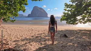 Back view woman walking towards tropical sandy beach island at sunset. Travel video of woman relaxing and enjoying beach paradise during summer holiday