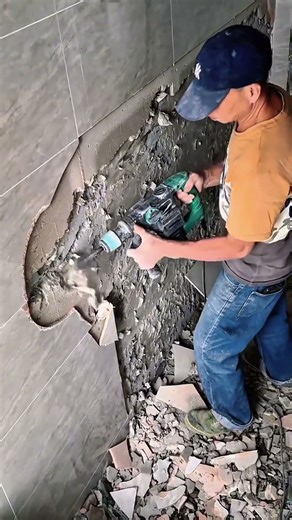 He breaks the wall tiles to redo the damaged area and prepare the surface for proper repair work