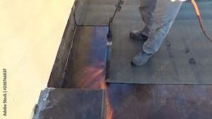 Worker performs sealing overlapping bitumen sheets on the flat roof of the building.