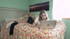 Full shot of young woman using computer and phone while lying in bed