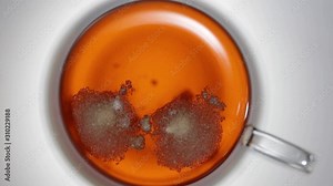 Top view video of cup with tea and two cubes of dissolving sugar.