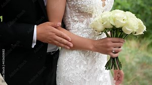 Young bride and groom hug and hold hands. The newlyweds caress each other's hands. Wedding bouquet in the hands of the bride.