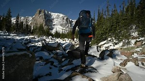 Hiker navigates through snow covered boulders off trail, Notchtop Mountain in the background, fall time, Rocky Mountain National Park, Colorado, USA