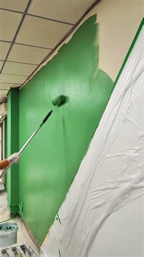 Painting the interior wall with vibrant green color using a long-handled paint roller
