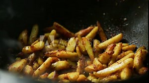 Pieces of potatoes are fried in oil in a cast-iron frying pan with a round bottom, steam comes, the oil boils. Cooking potatoes in Kazan, close-up