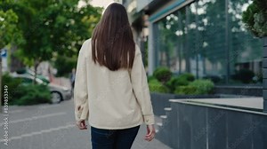 Rear view of a woman walking along an urban street surrounded by greenery and modern buildings. Perfect for concepts of urban living, outdoor activity, and daily commute. Woman Walking In Urban Street