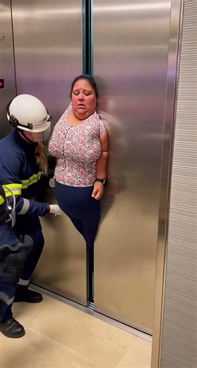 An extremely obese adult woman is wedged tightly between partially closed metal elevator door