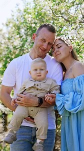 Happy Caucasian couple with their adorable little baby. Loving family of three in the garden in spring. Vertical video.